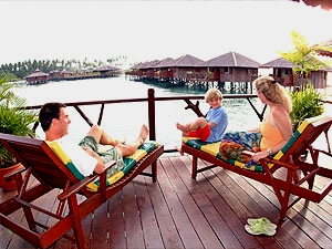 Guests on sun loungers on the private deck of a Grand Deluxe chalet, looking over the water chalets